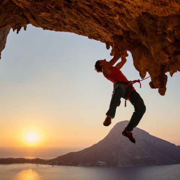 Man rock climbing on an overhang at sunset, demonstrating strength, endurance, and resilience. A powerful representation of mobility, functional movement, and body control—key aspects of movement training at Renew Strength and Wellness.